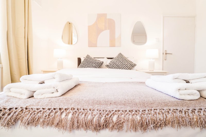 Minimalist bedroom with bed, white bedding, folded towels, and neutral wall art