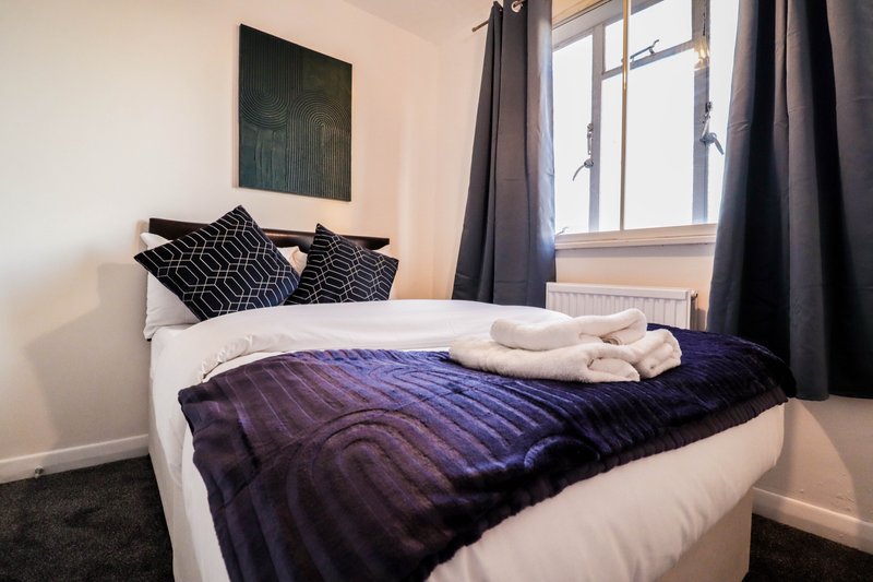 Modern bedroom with double bed, purple duvet, black patterned cushions and dark curtains