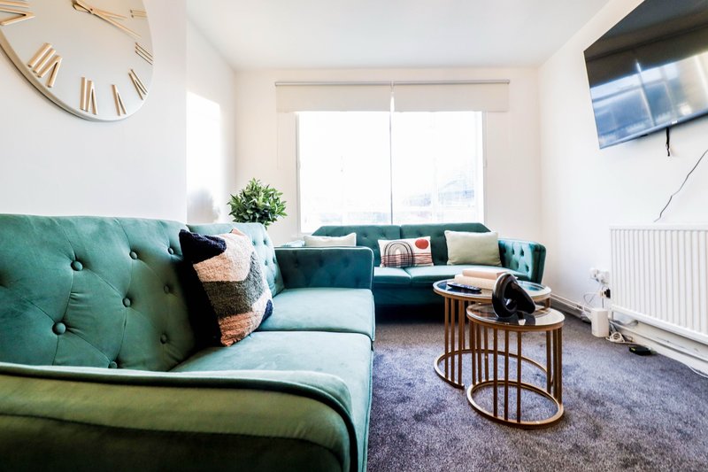 Bright living room with green upholstered sofa, wooden side table, potted plant and large window