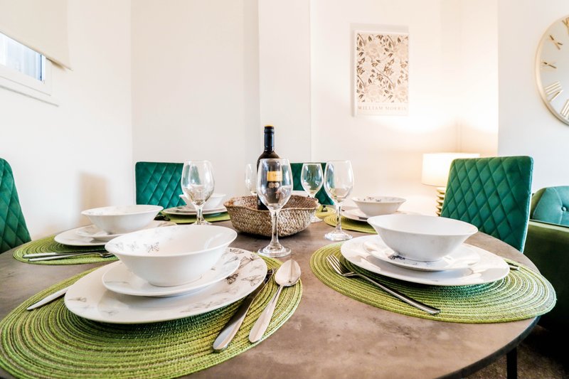 Dining table set for four with white plates, green placemats, wine bottle and glasses