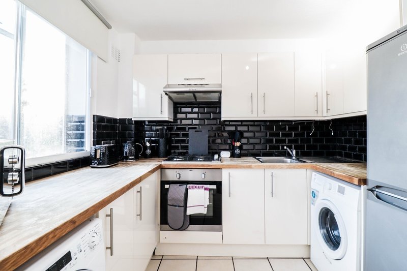 Modern kitchen with white cabinets, black tile backsplash, wooden countertops and integrated appliances