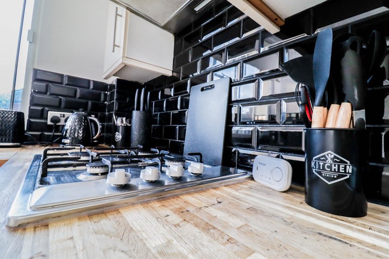 Modern kitchen with black subway tile, wooden countertop, shelving, and kitchen utensils