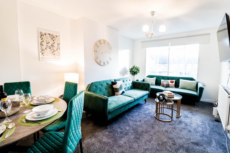 Modern open-plan living and dining area with teal sofa, dining table, and large windows