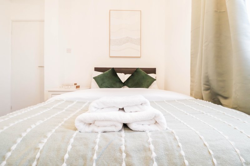 Bright bedroom with striped bedding, green cushions, framed wall art, and folded towels on bed