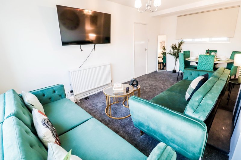 Modern living room with turquoise sofas, wall-mounted TV, and dining area in background