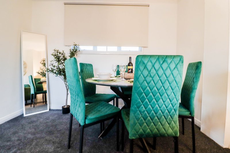 Dining area with round black table, four quilted green chairs, and full-length mirror