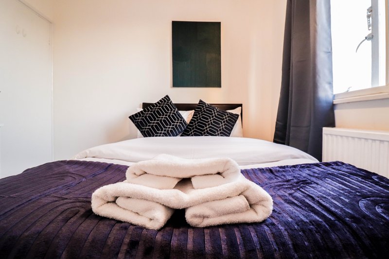 Bedroom with double bed, rolled towels, geometric cushions and framed artwork on wall