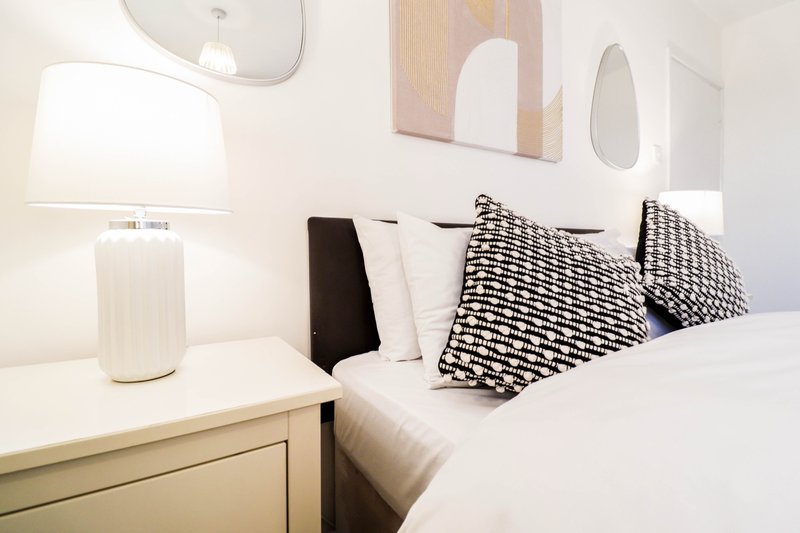 Modern bedroom with double bed, geometric patterned pillows, bedside lamp and mirror