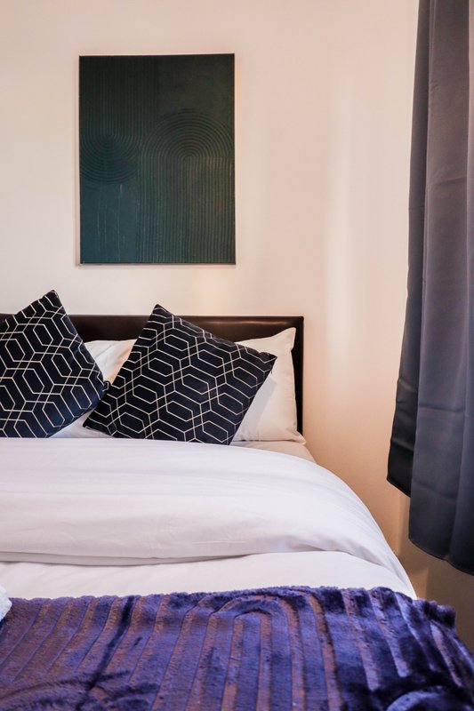 Modern bedroom with double bed, patterned pillows, white bedding, and framed wall art