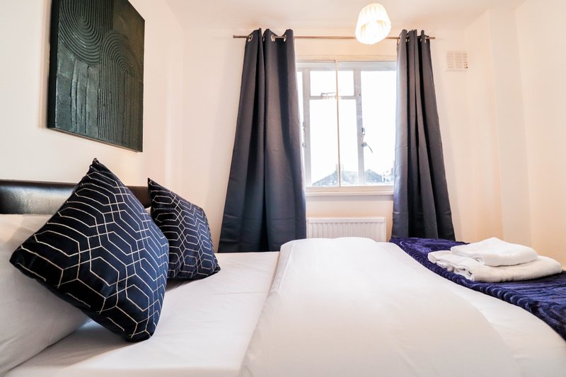Bright bedroom with two single beds, patterned pillows, dark curtains and window