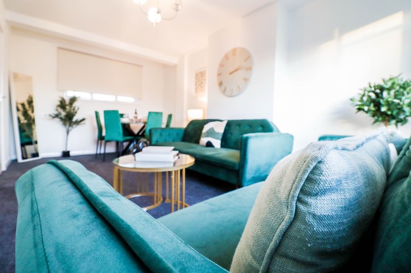Modern living room with teal sofas, round coffee table, wall clock and potted plants