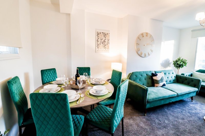 Open-plan living and dining area with teal upholstered chairs, round wooden table, and matching sofa