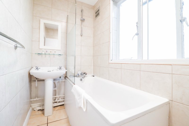 Bathroom with pedestal sink, bathtub, white tile walls and window