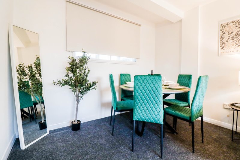 Modern dining area with turquoise upholstered chairs, dark table, potted plant, and leaning mirror