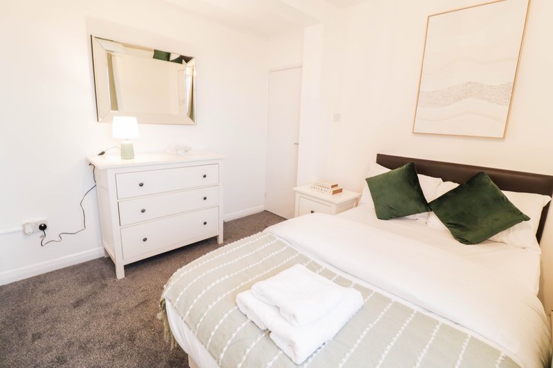 Bright bedroom with double bed, white dresser, mirror and framed wall art
