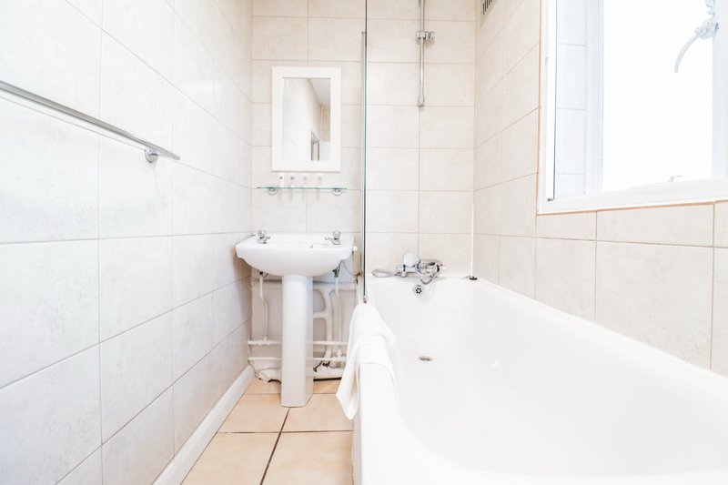 Clean bathroom with white bathtub, pedestal sink, tiled walls and mirror