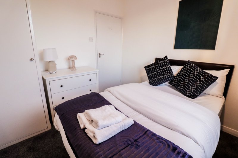 Bedroom with double bed, white bedding, patterned pillows, white dresser and black artwork