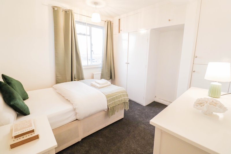 Bright bedroom with single bed, green cushion, desk, wardrobe and window with curtains