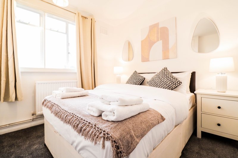 Bright bedroom with double bed, rolled towels, white bedding, wooden nightstand and wall art