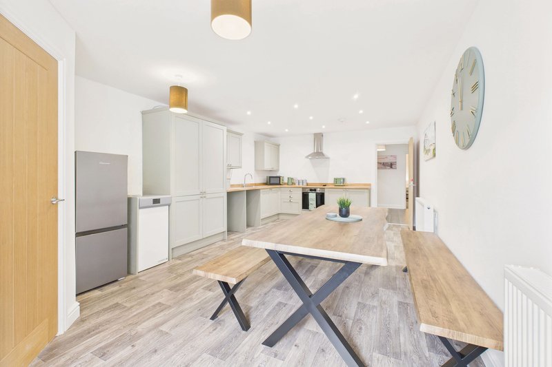 Modern open-plan kitchen and dining area with white cabinetry, wooden dining table, and stainless steel appliances