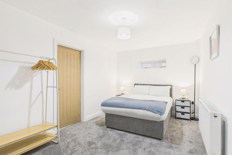Bedroom with double bed, bedside tables, wooden wardrobe and grey carpet flooring