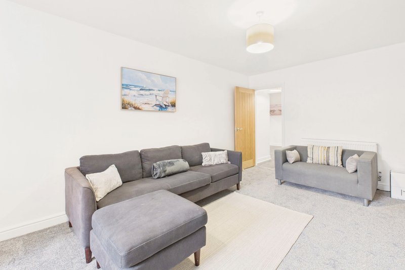 Living room with grey sectional sofa, ottoman, cushions, and wooden door