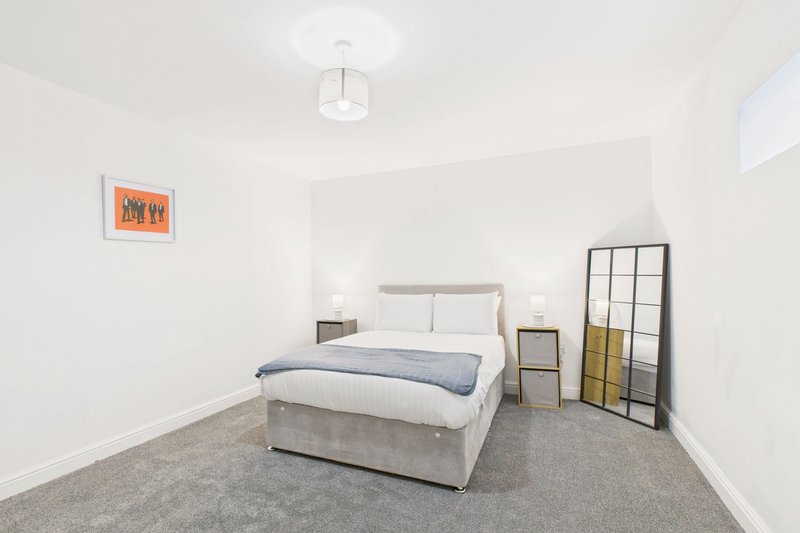 Bright modern bedroom with double bed, grey carpet, white walls and minimalist furnishings