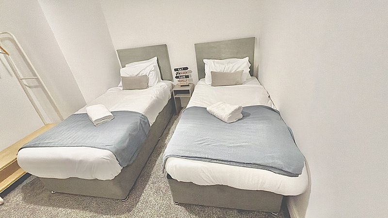 Twin bedroom with two single beds, grey headboards, white bedding and neutral walls