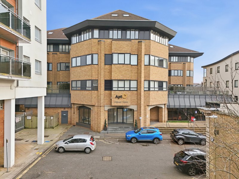 Brick apartment building with ground-floor commercial space and parked cars in courtyard