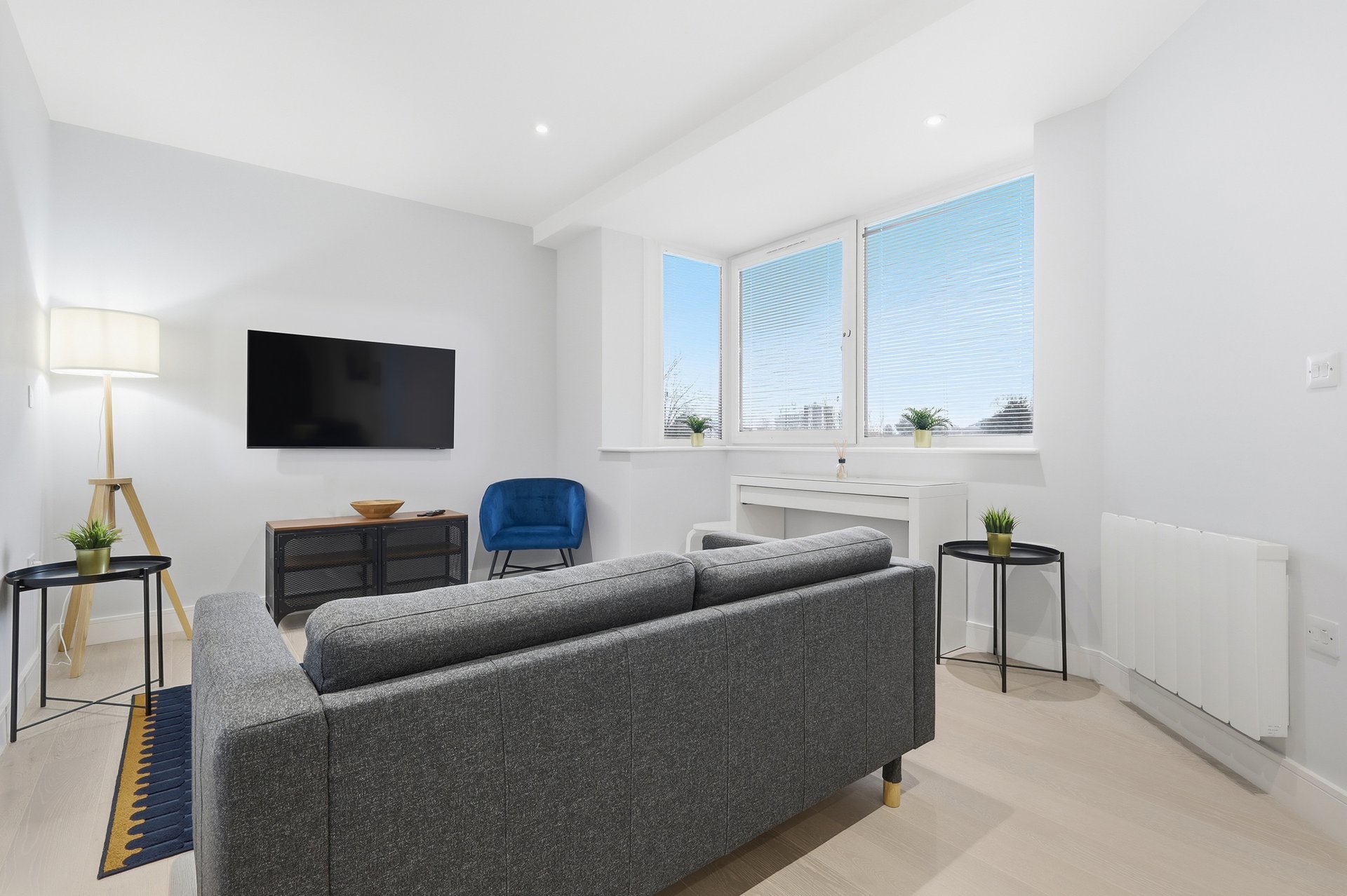 Modern living room with gray sofa, wall-mounted TV, blue chair and large windows with city views