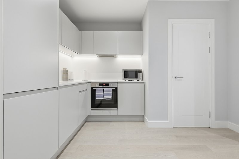 Modern kitchen with white cabinetry, built-in oven, light wood flooring and white door