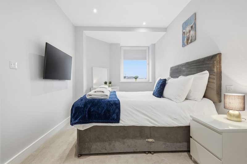Modern bedroom with double bed, blue throw, wall-mounted TV and ensuite bathroom view