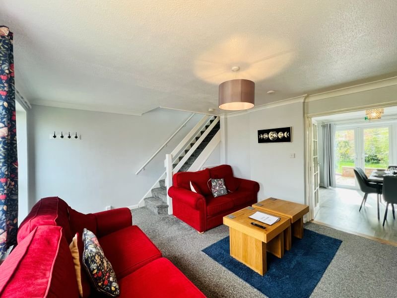 Modern living room with two red velvet sofas, wooden coffee table, and staircase leading upstairs