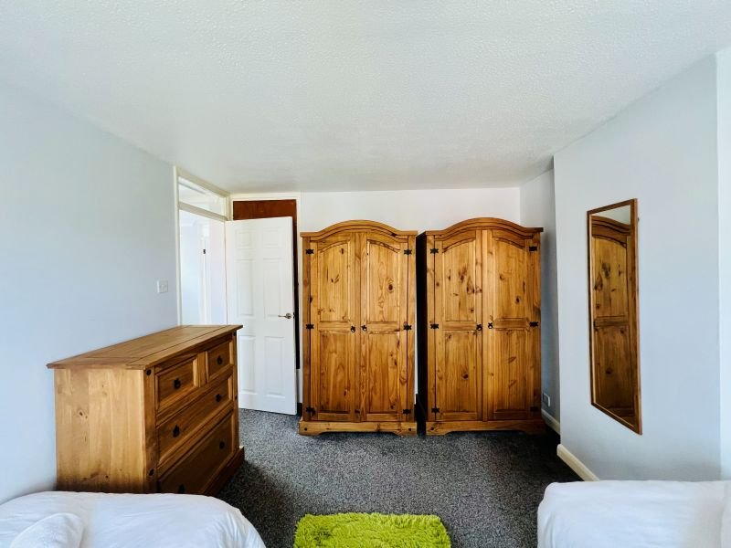 Bedroom with two single beds, wooden wardrobe and chest of drawers, white walls