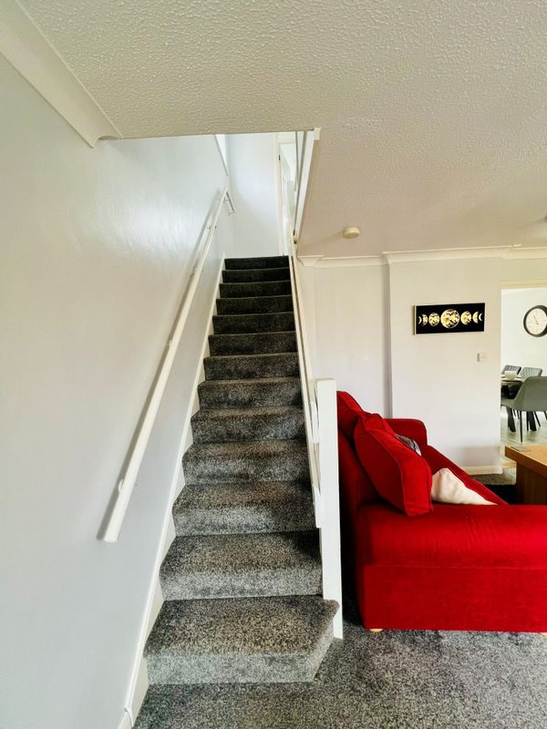 Staircase with gray carpet and white walls, red sofa visible in foreground