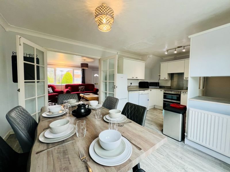 Open-plan kitchen and dining area with wooden table, place settings, and view to living room