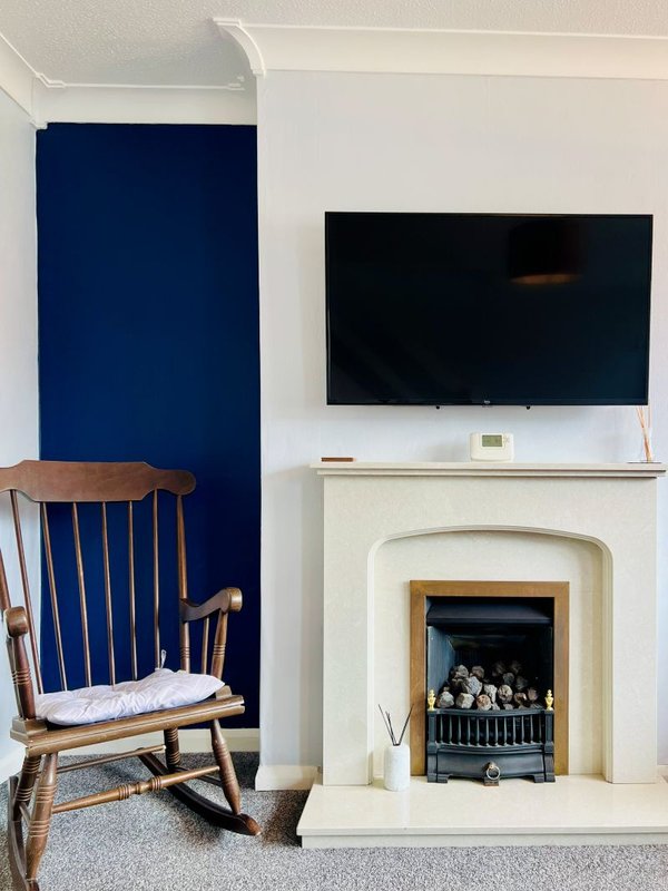 Living room with wooden armchair, fireplace with electric insert, wall-mounted TV, and blue accent wall