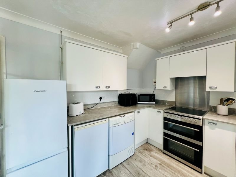 Modern kitchen with white cabinets, stainless steel appliances, and wooden-effect flooring