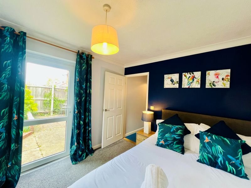 Bedroom with double bed, dark blue accent wall, teal patterned curtains and cushions, pendant light