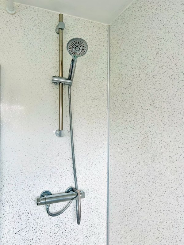 Bathroom shower wall with chrome thermostatic mixer and handheld showerhead