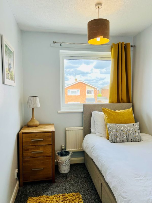 Small bedroom with single bed, wooden bedside table, pendant lamp and window view