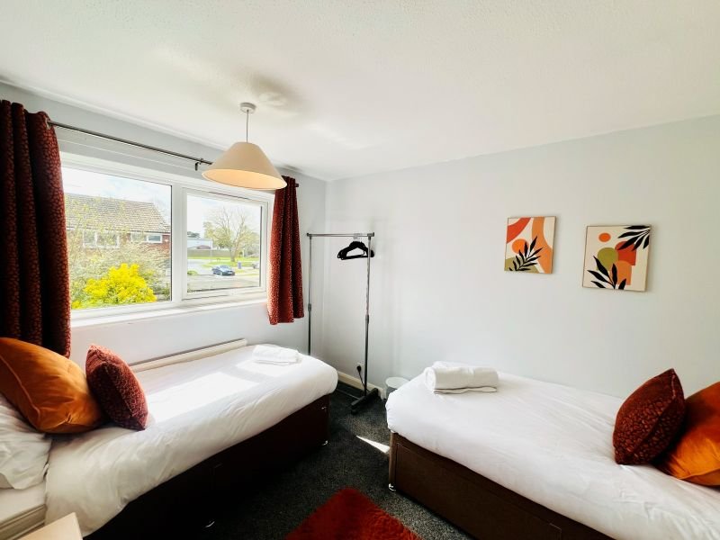 Bright twin bedroom with two single beds, burgundy cushions, pendant lamp and garden views