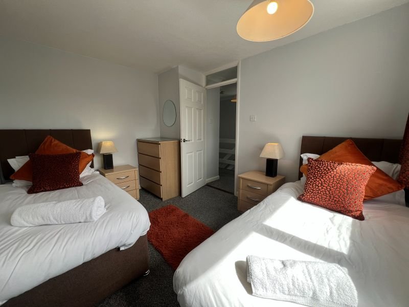 Twin bedroom with two single beds, burgundy cushions, wooden furniture and ensuite door