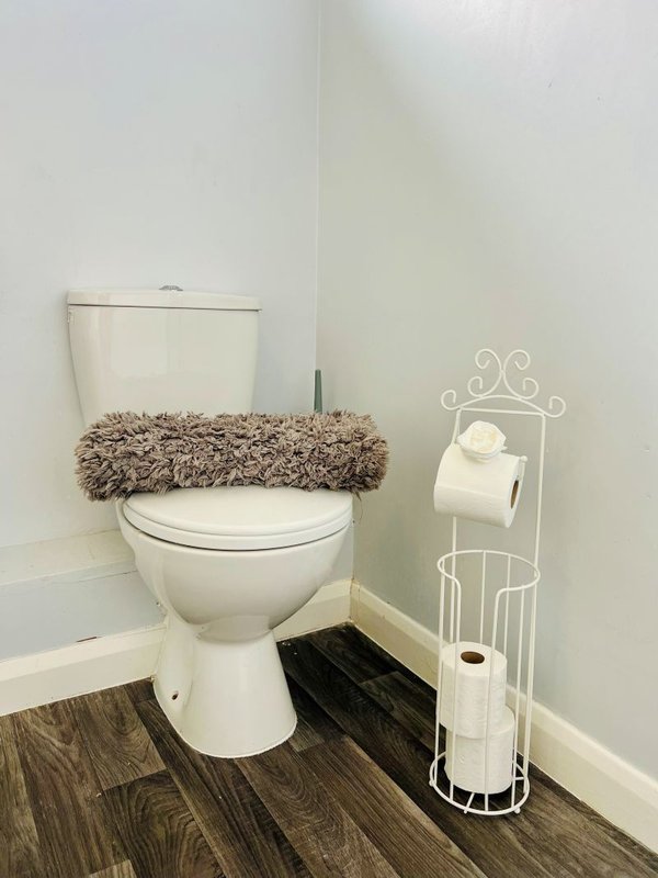 Bathroom with white toilet, fuzzy seat cover, dark wood-effect flooring and white metal toilet paper holder