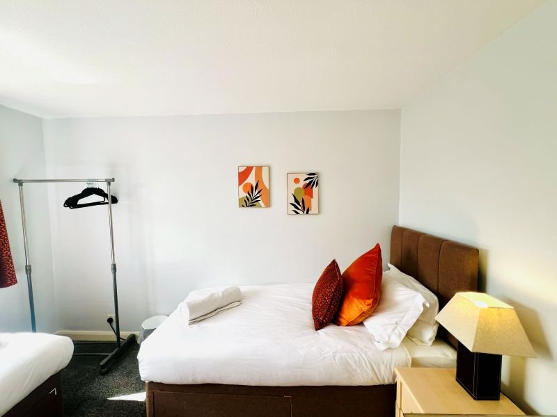 Bedroom with double bed, red and gold pillows, wooden headboard, bedside lamp and wall art