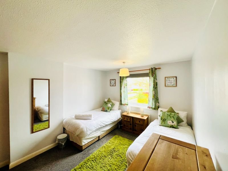 Bright twin bedroom with two single beds, wooden furniture, green accents and window with plants