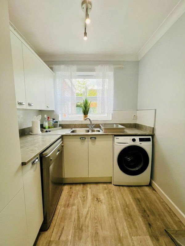 Small kitchen with cream cabinets, stainless steel sink, washing machine and window with potted plant