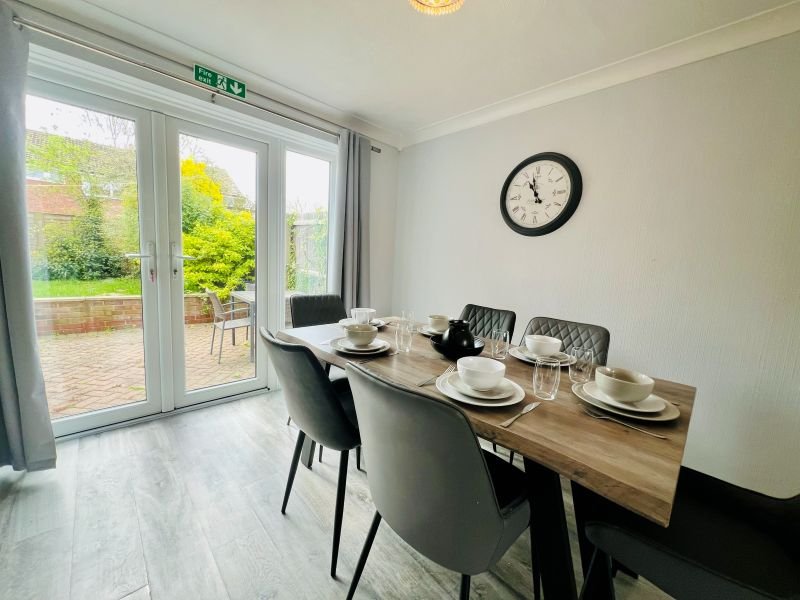 Modern dining room with wooden table, black chairs, wall clock, and patio doors overlooking garden