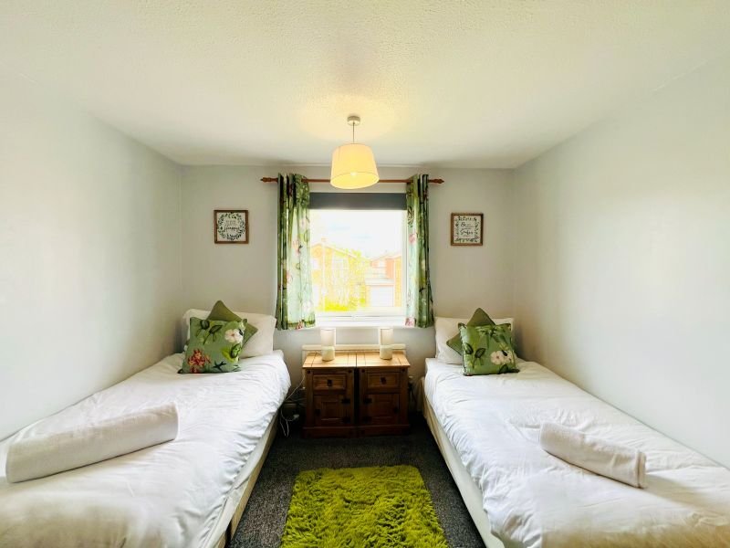 Twin bedroom with two single beds, window with green curtains, pendant light and potted plants