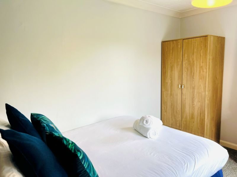 Bedroom with double bed, blue and green cushions, wooden wardrobe, and yellow pendant light